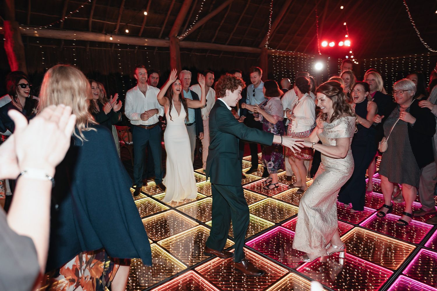 Guests dancing on illuminated LED dance floor at elegant barn wedding reception with string lights.