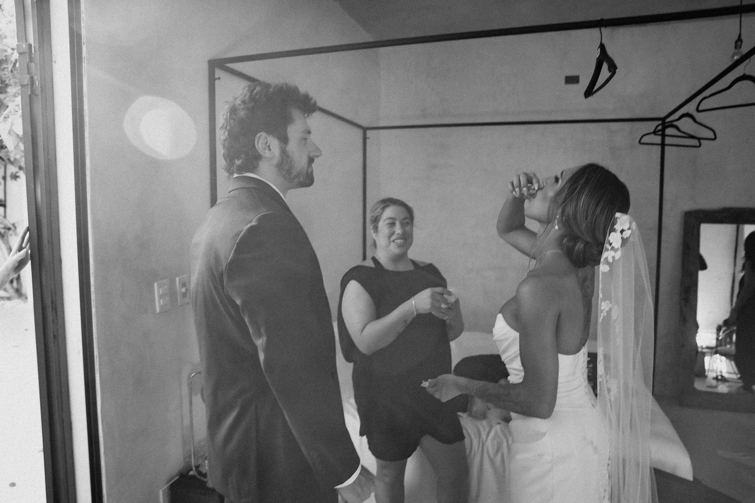Black and white photo of bride and groom sharing an intimate moment with wedding coordinator in dressing room.