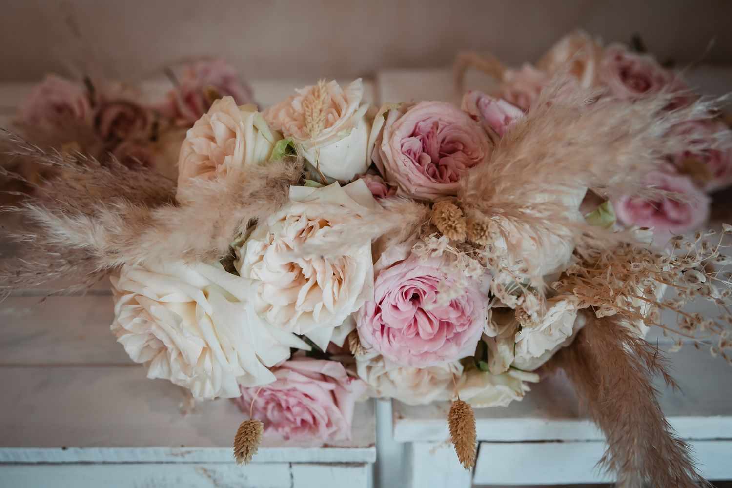 Romantic wedding bouquet with blush pink roses and pampas grass in soft peach and cream tones.