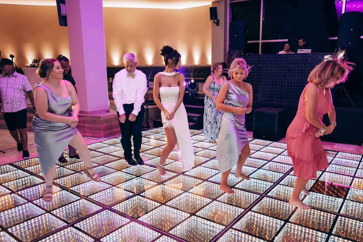 Wedding guests dancing on illuminated LED dance floor with purple ambient lighting.