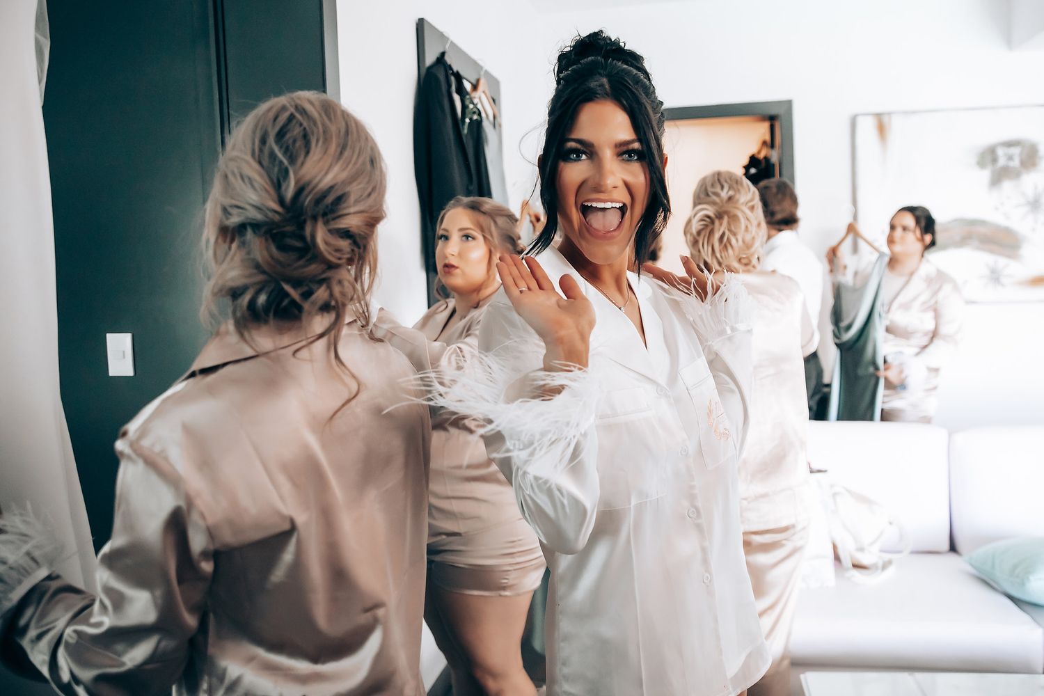 Candid moments of a bridal party getting ready in a bright room wearing white and beige outfits.