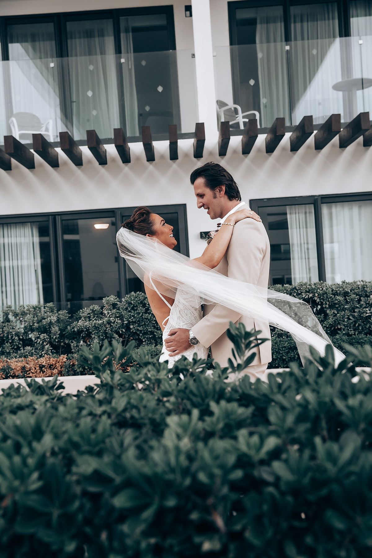 Wedding couple sharing intimate moments in a garden setting with flowing veil in the breeze.