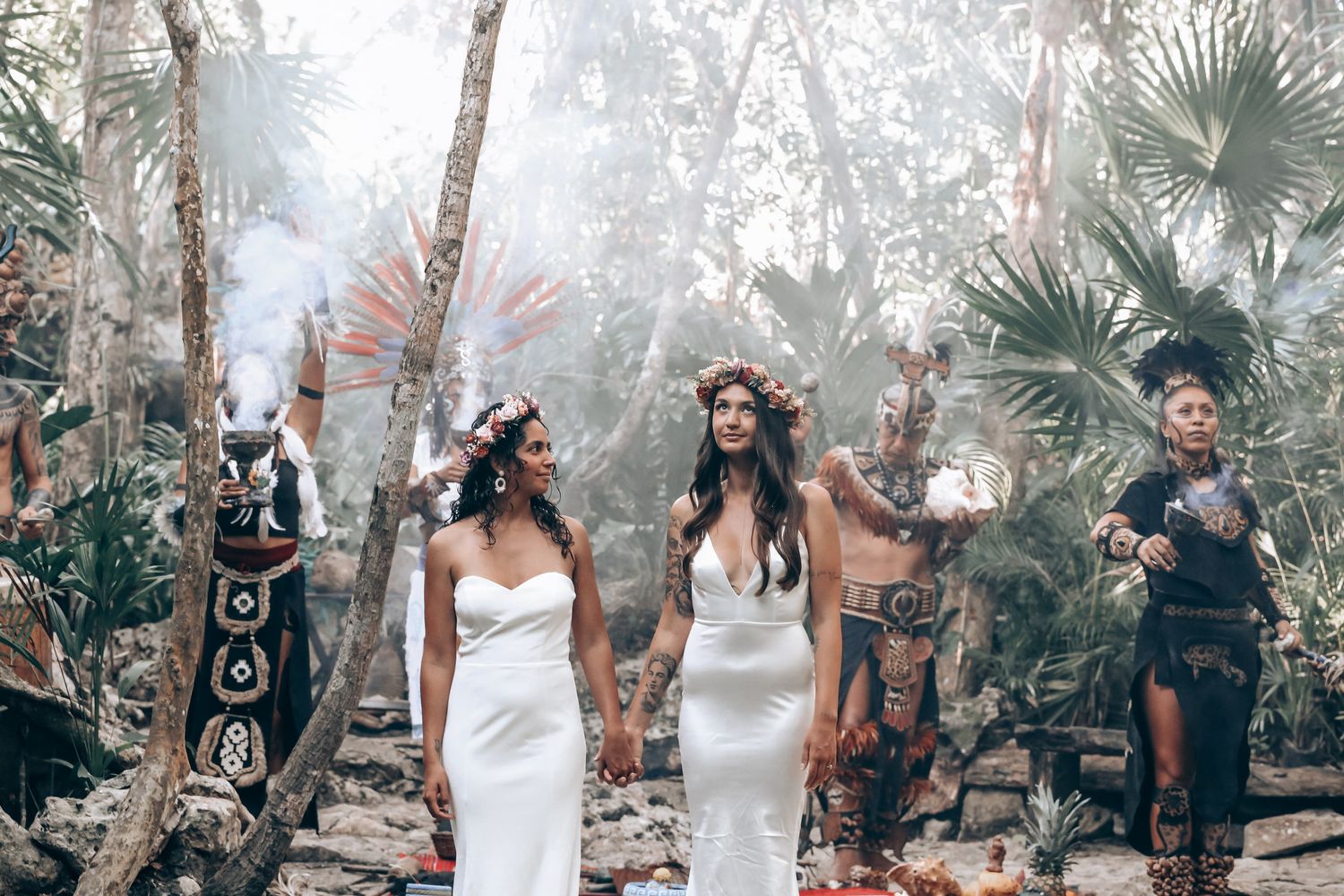 Wedding ceremony participants gather in a dreamy forest setting with palm trees and natural light filtering through.