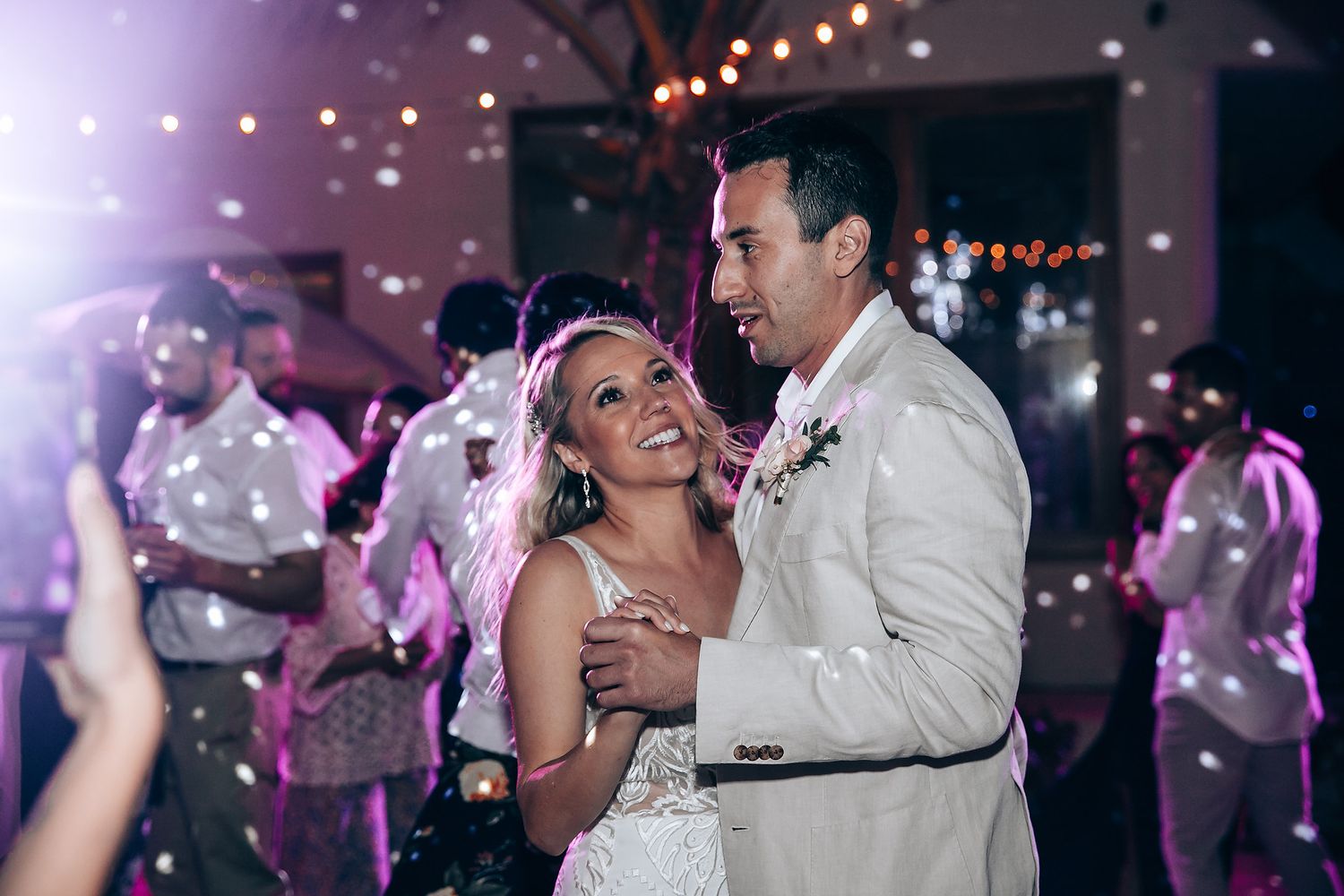 Festive dance floor scene with purple lighting and string lights overhead.