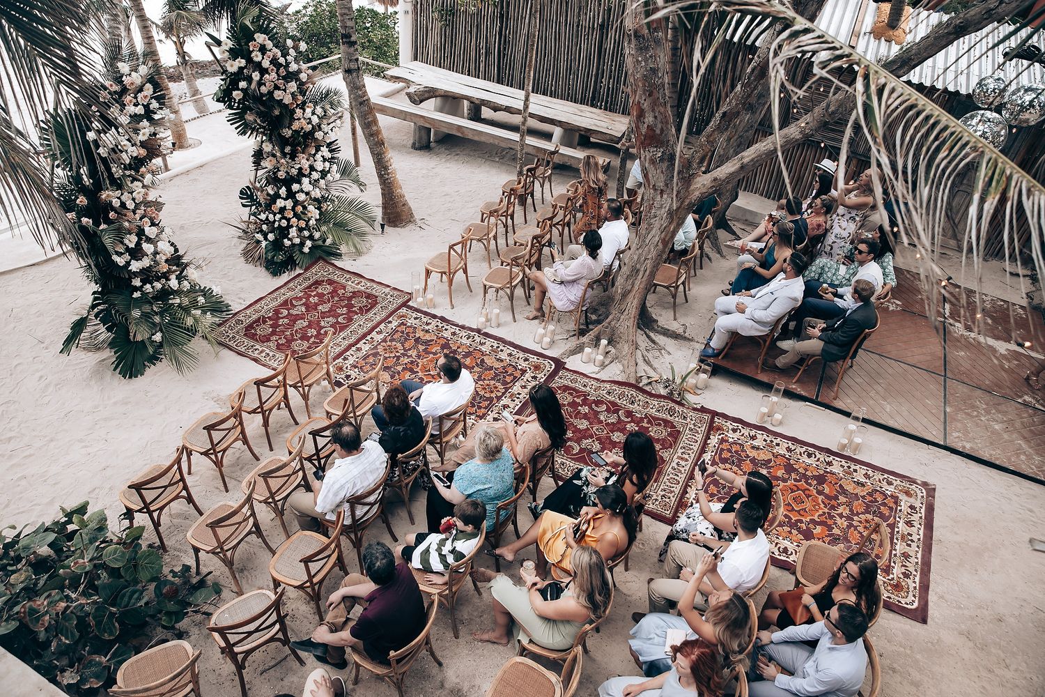 Wedding reception setup with rustic wooden chairs and tables decorated with greenery and flowers.