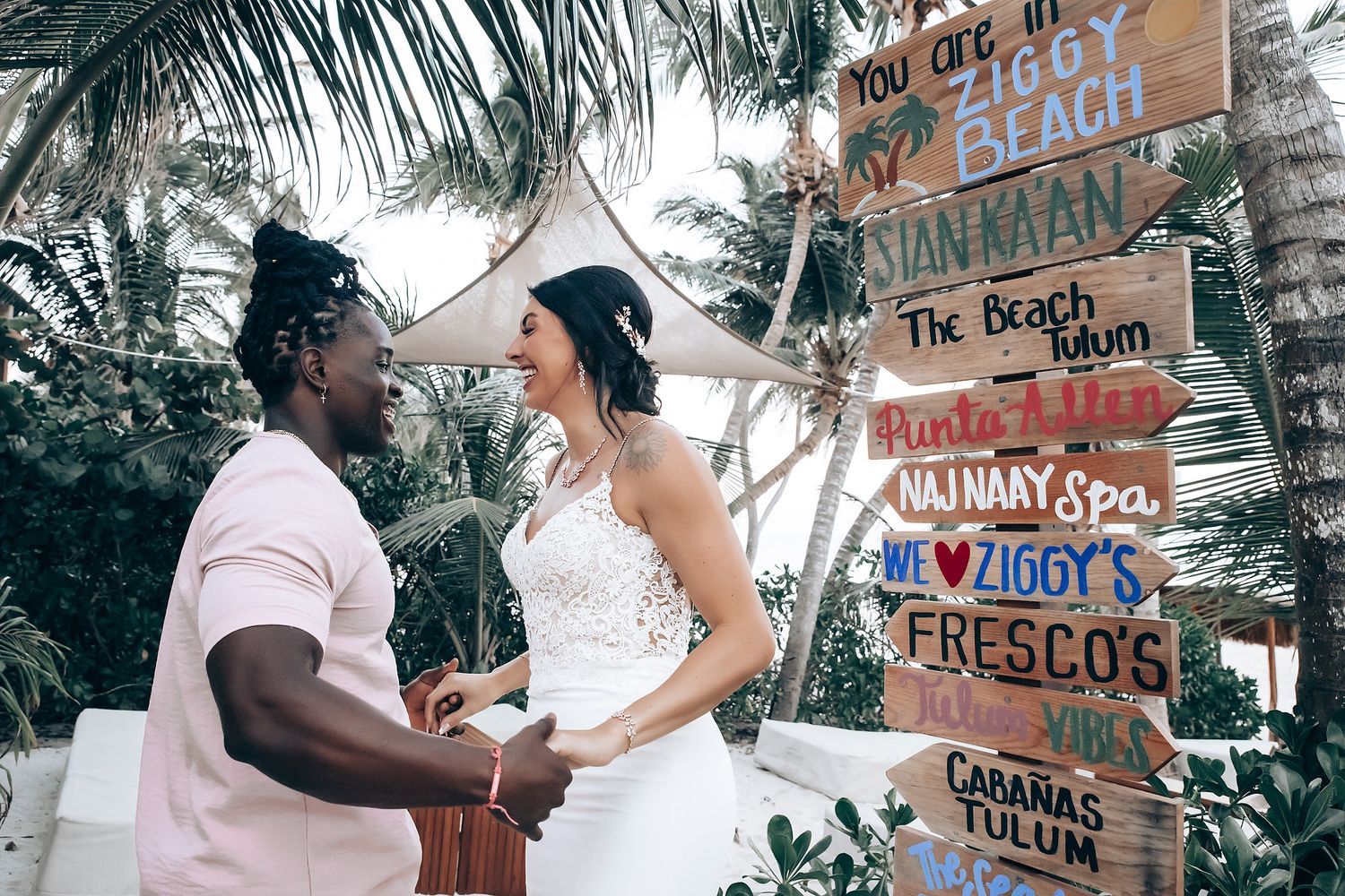 A bride and groom stand together on a beach with tropical decor.