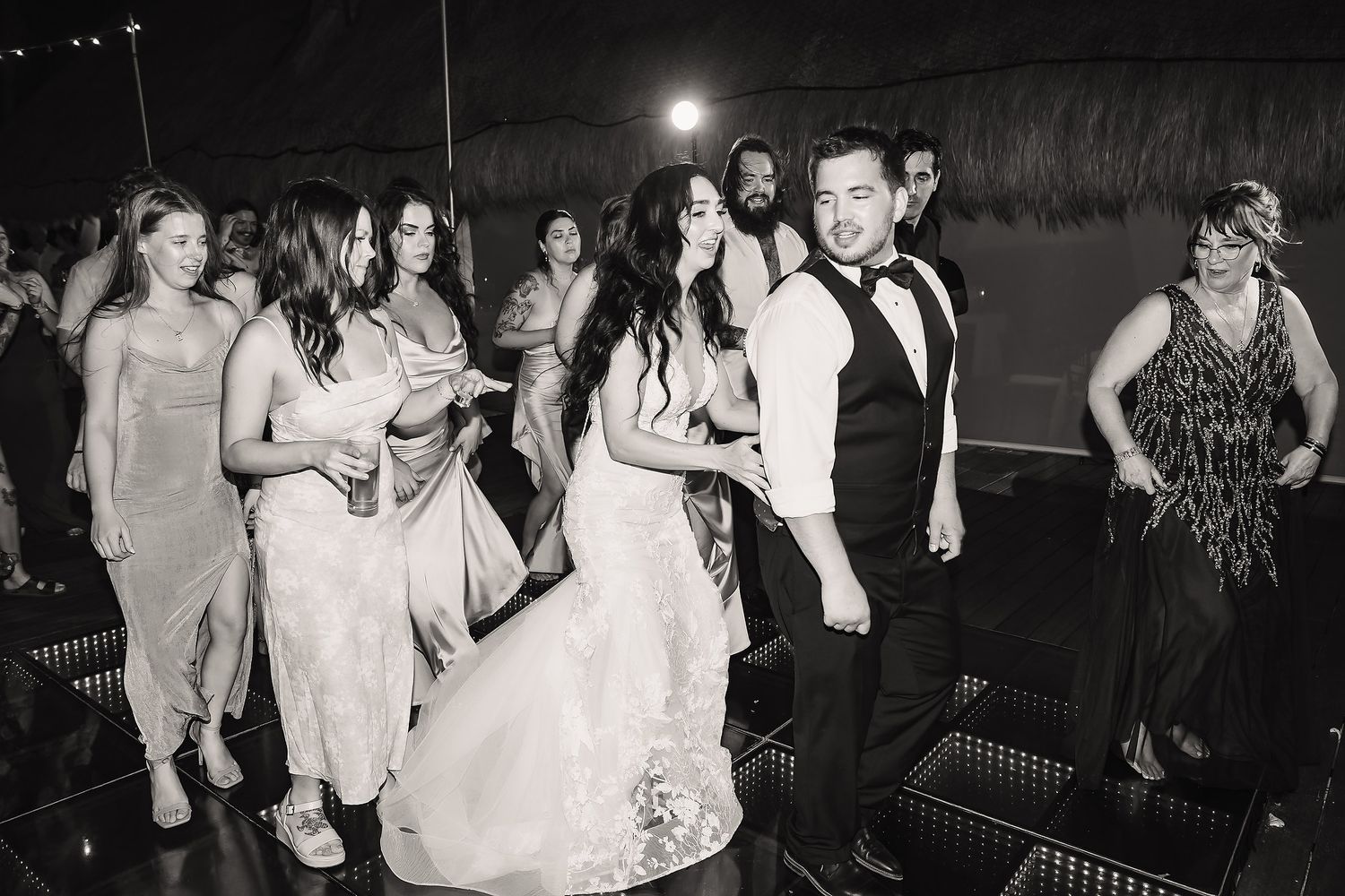 Black and white photo of bride and groom dancing with bridesmaids at elegant wedding reception party.