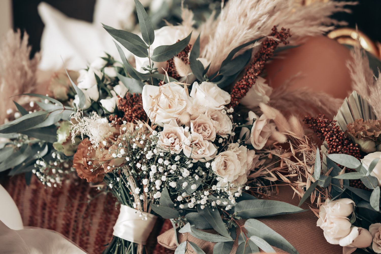 Elegant bridal bouquet with white roses, baby's breath, eucalyptus, and dried pampas grass in warm neutral tones.