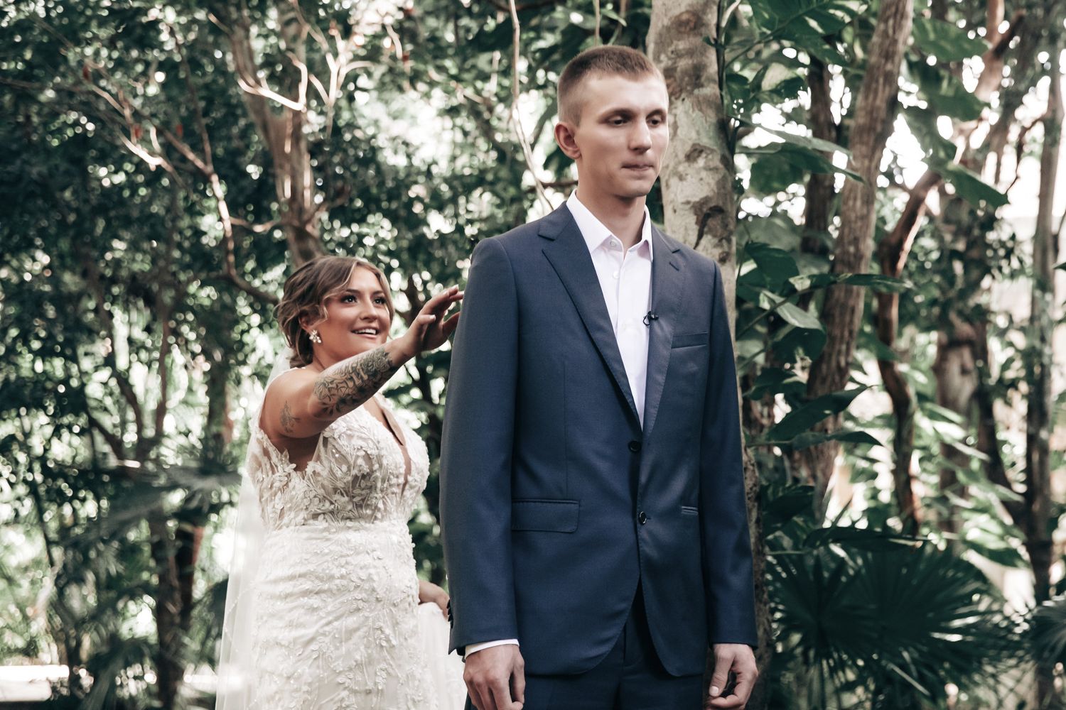 Bride surprising groom during emotional first look moment in lush tropical garden setting.