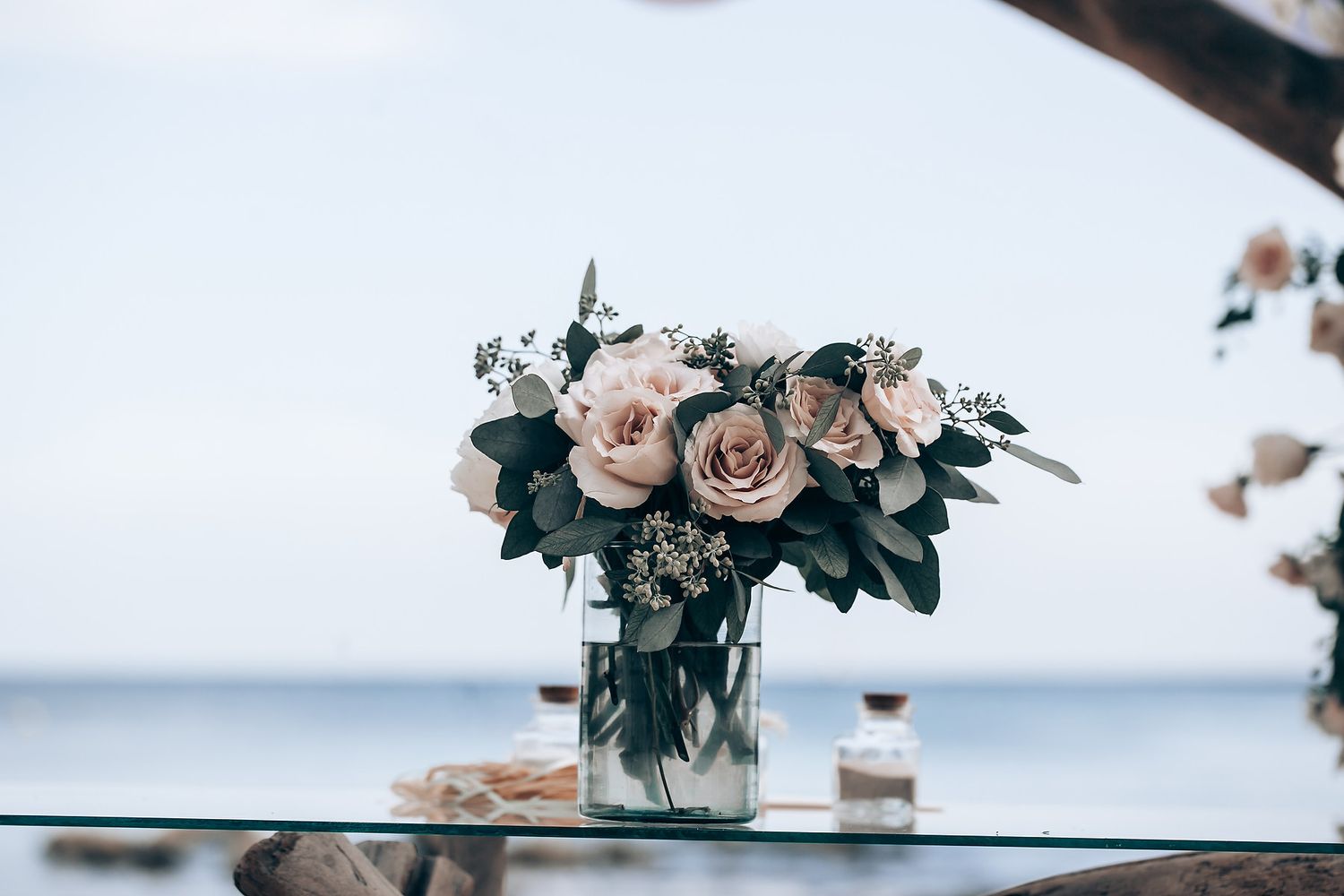 Elegant floral arrangements with pink roses and greenery decorating a seaside wedding venue.