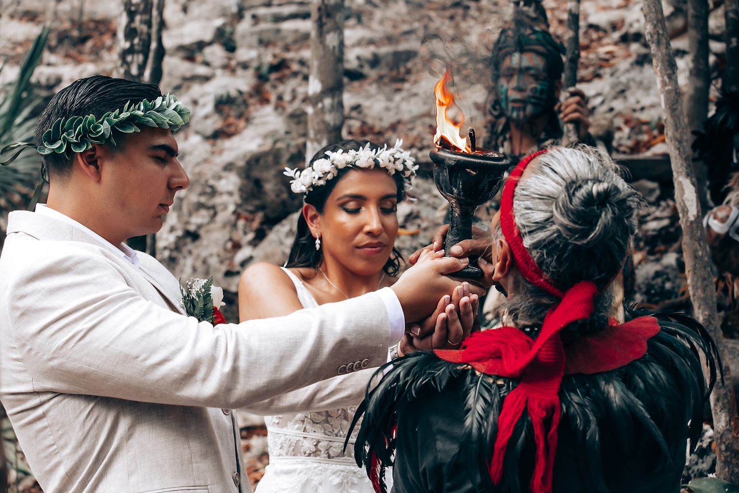 A ceremonial ritual being performed near a stone statue draped in red fabric during an outdoor wedding.