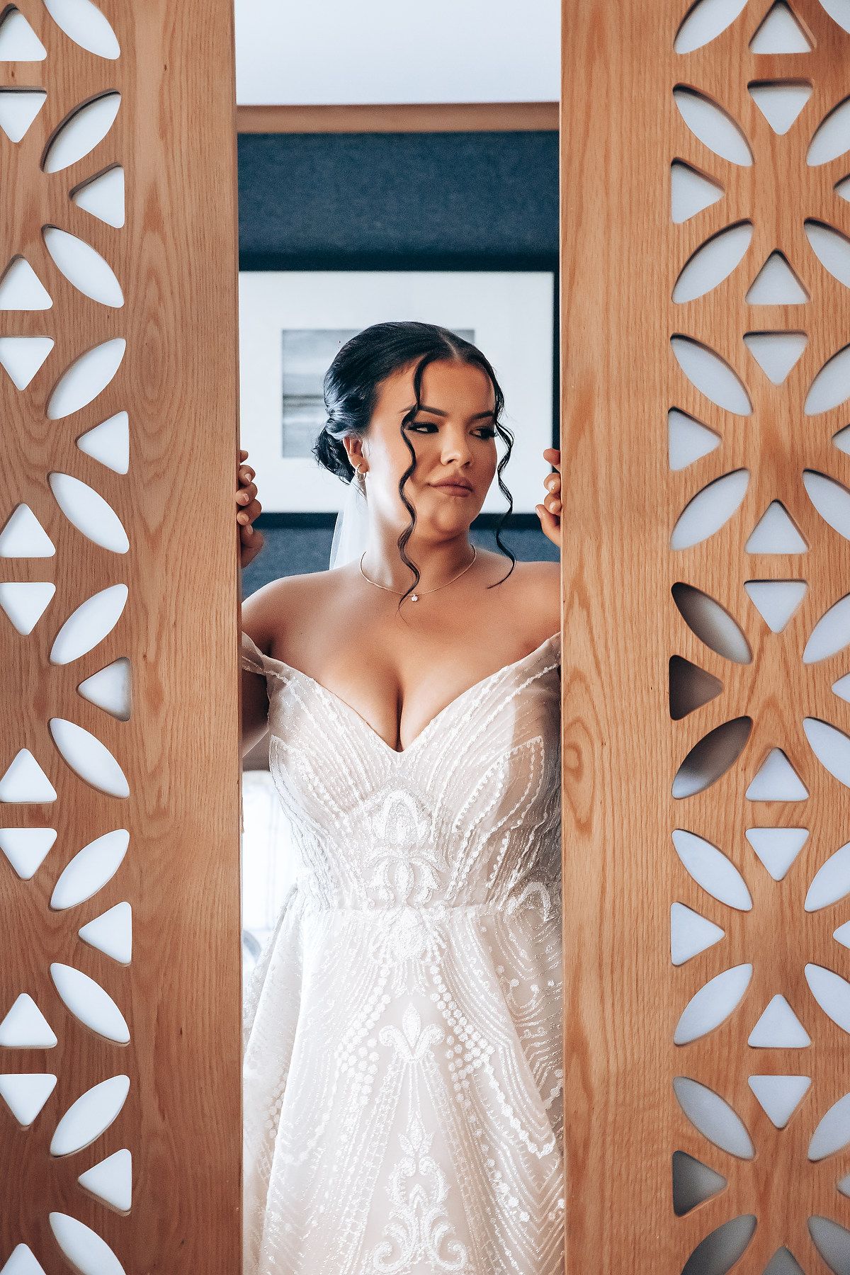 A white lace wedding dress with sweetheart neckline viewed through decorative wooden panels with floral cutout design.