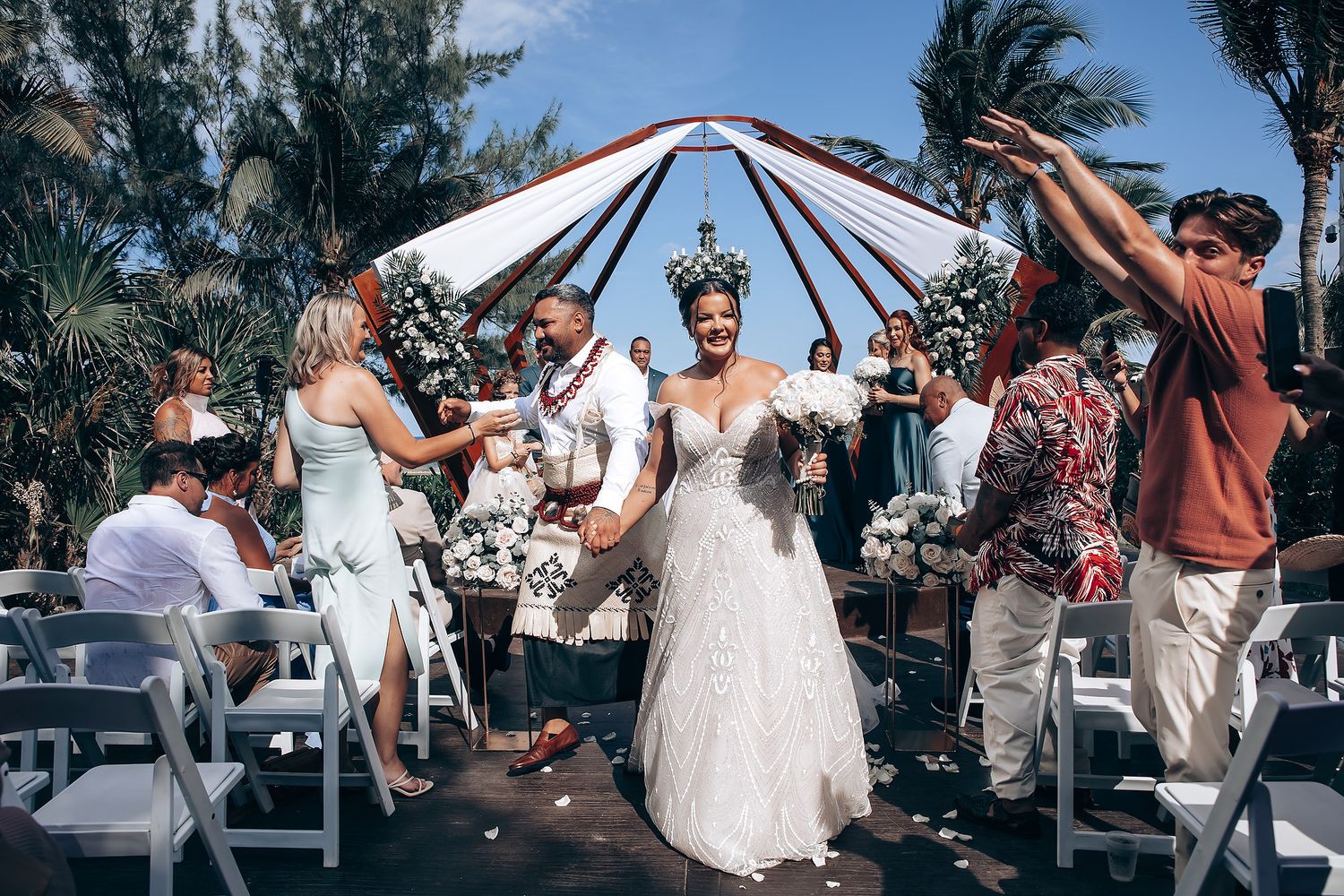 Wedding celebration with guests dancing under a wooden pavilion by the beach.