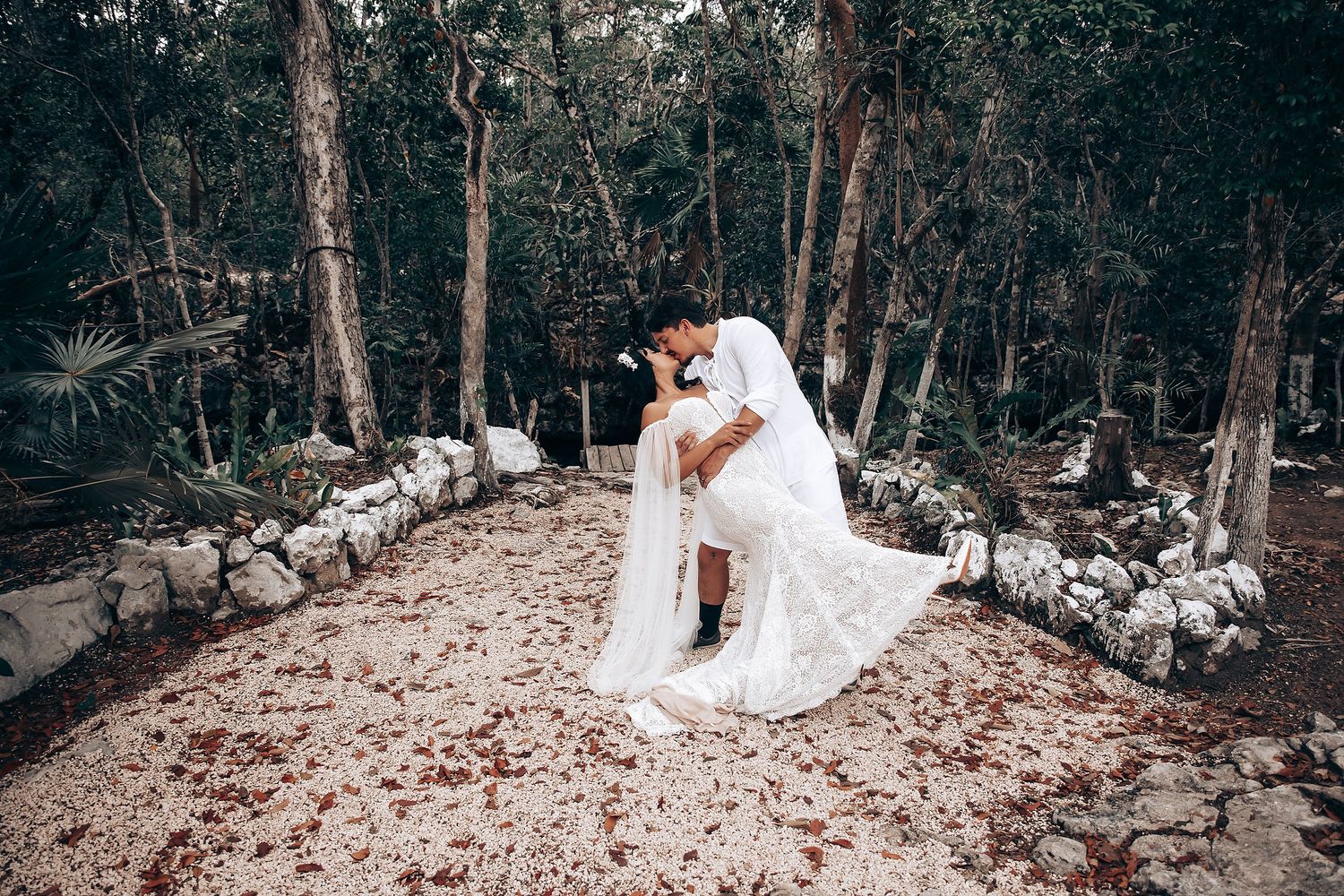 A romantic wedding couple shares intimate moments in a rustic forest setting with stone walls and fallen leaves.