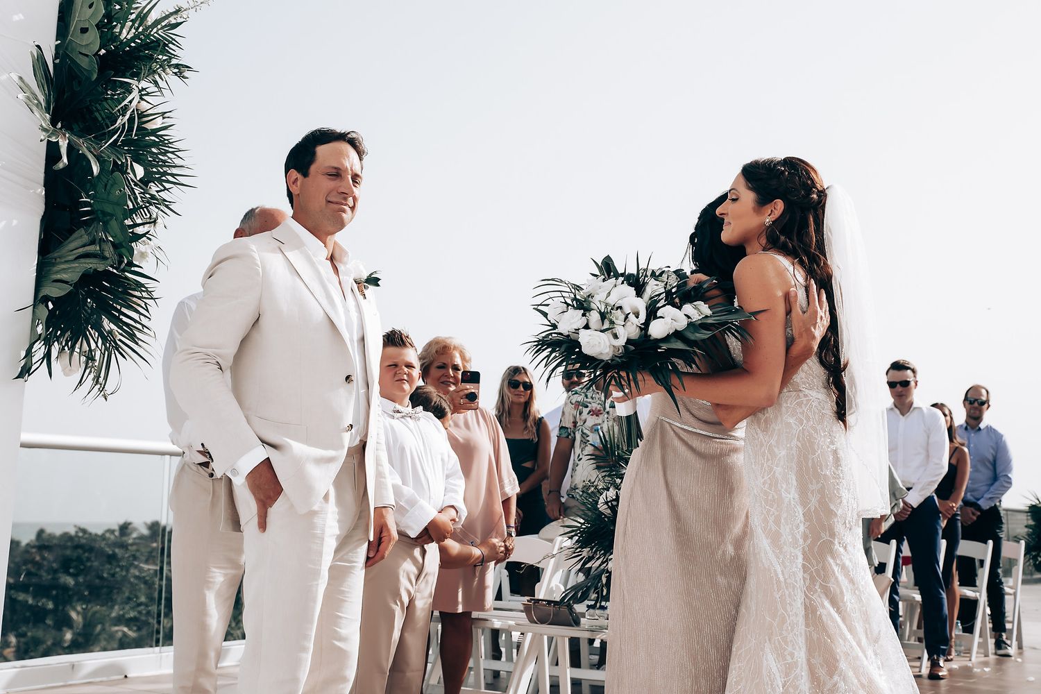 Wedding celebration with guests in light colored outfits dancing under tropical palm decorations.