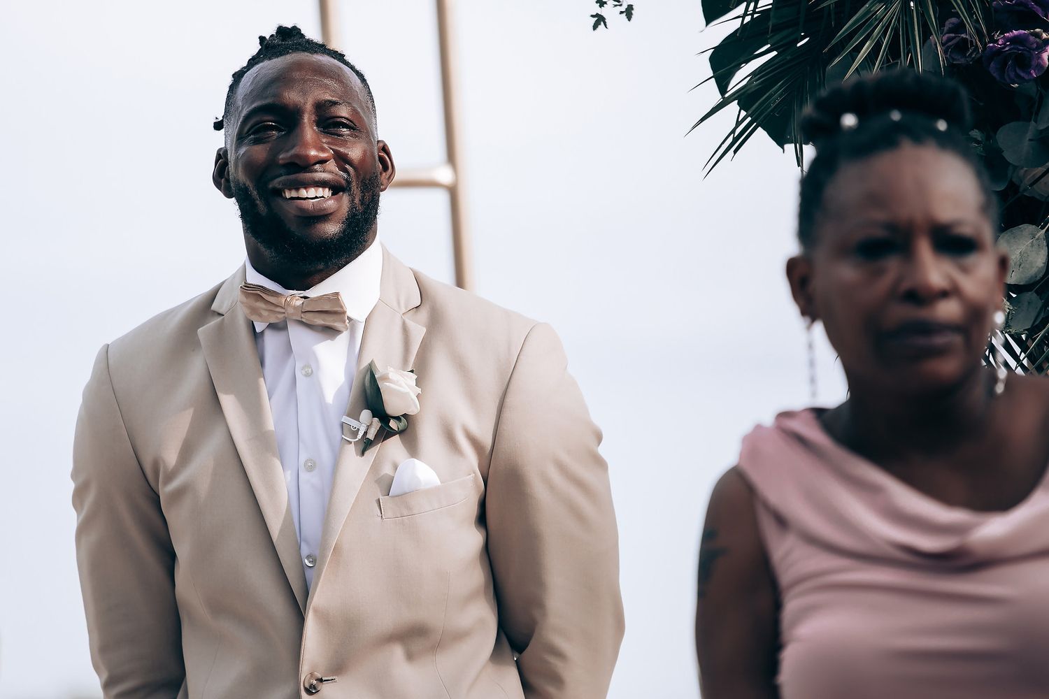 Wedding party members in light beige suits posing against white backdrop.