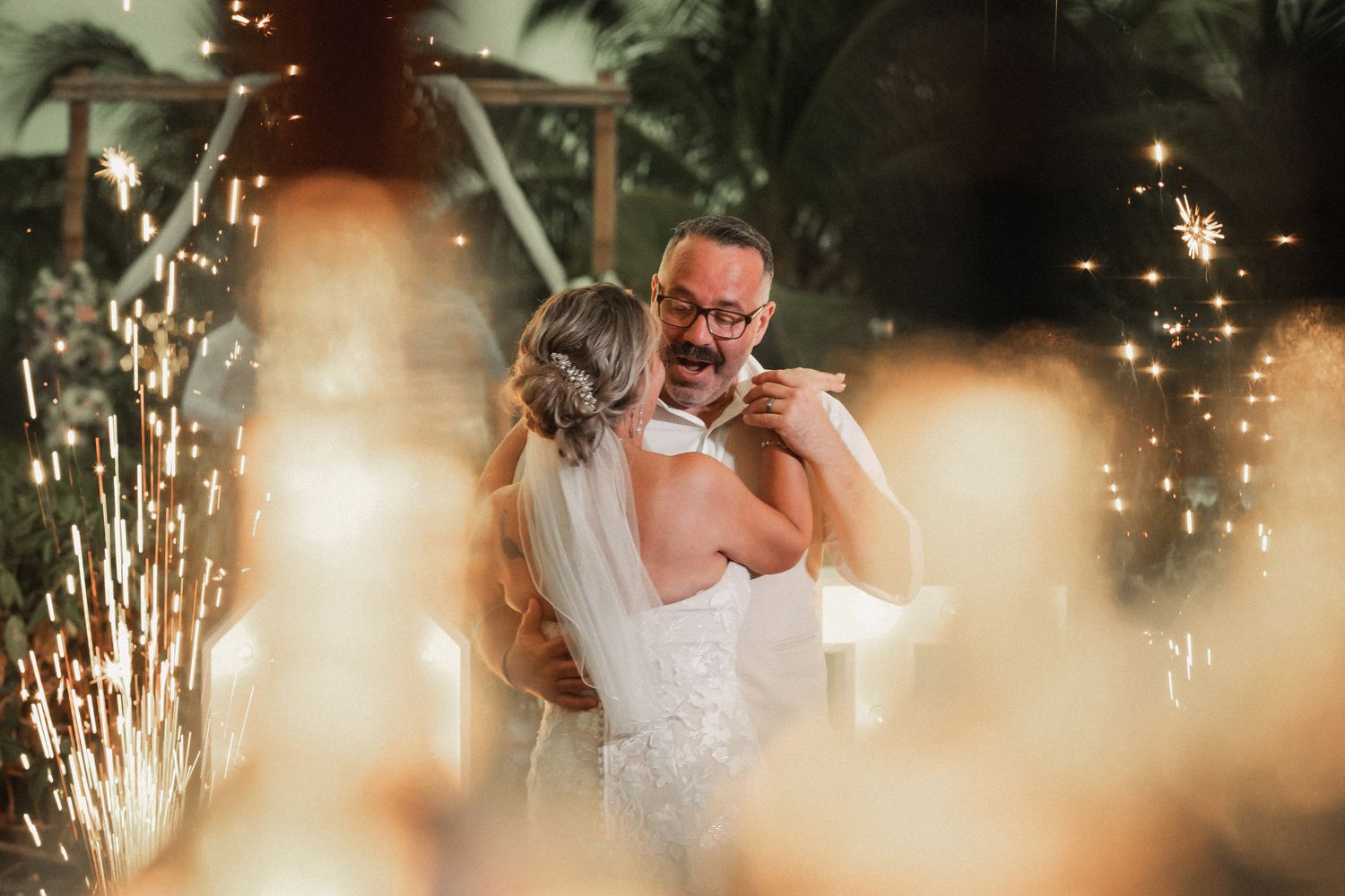 Couple shares emotional first dance surrounded by sparkling fireworks at romantic wedding reception.