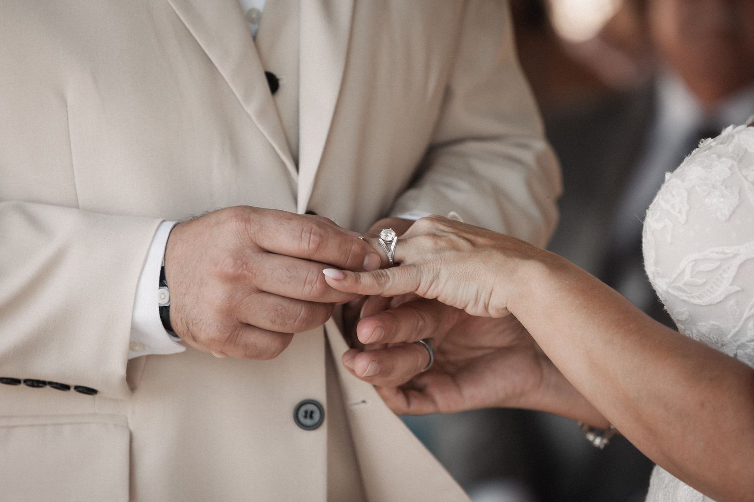 Close-up of groom placing diamond engagement ring on brides finger during wedding ceremony.