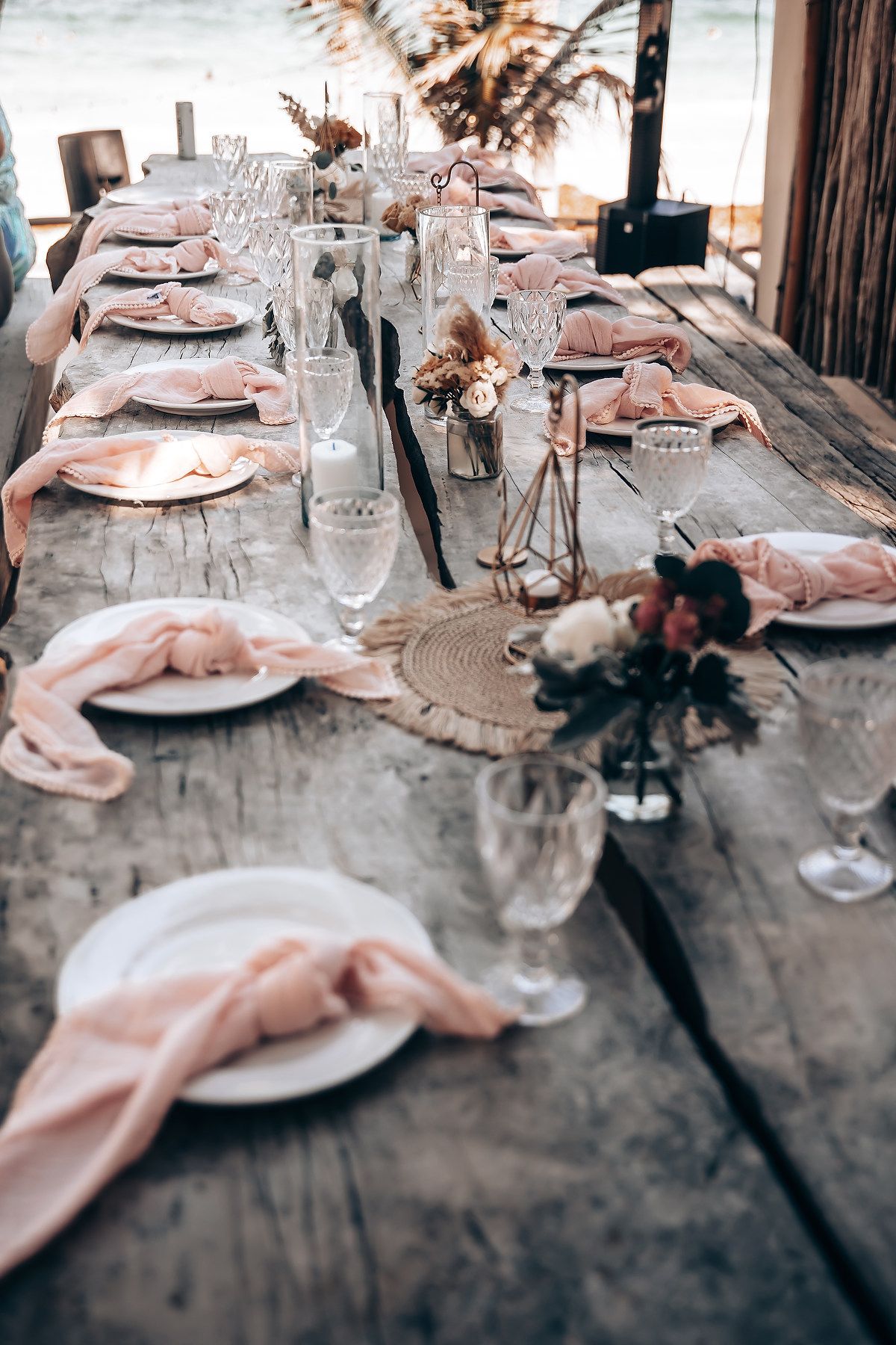 Elegant table settings with pink napkins and crystal glasses at a rustic wooden table.