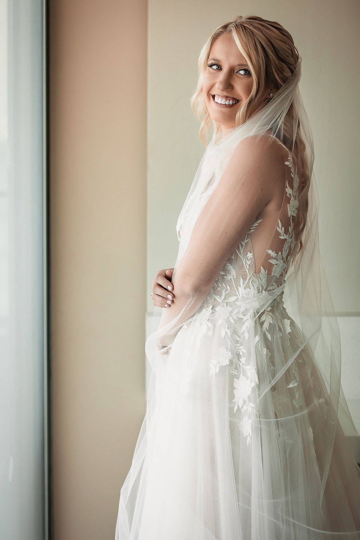 A flowing white wedding dress with delicate lace details captured in natural window light.