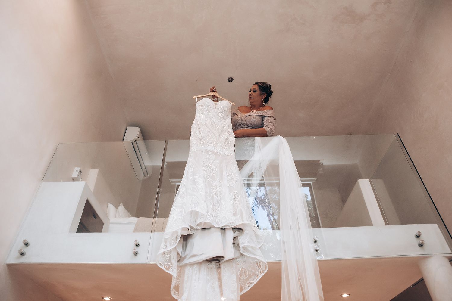 A wedding dress hangs elegantly from a high ceiling in a modern white interior.