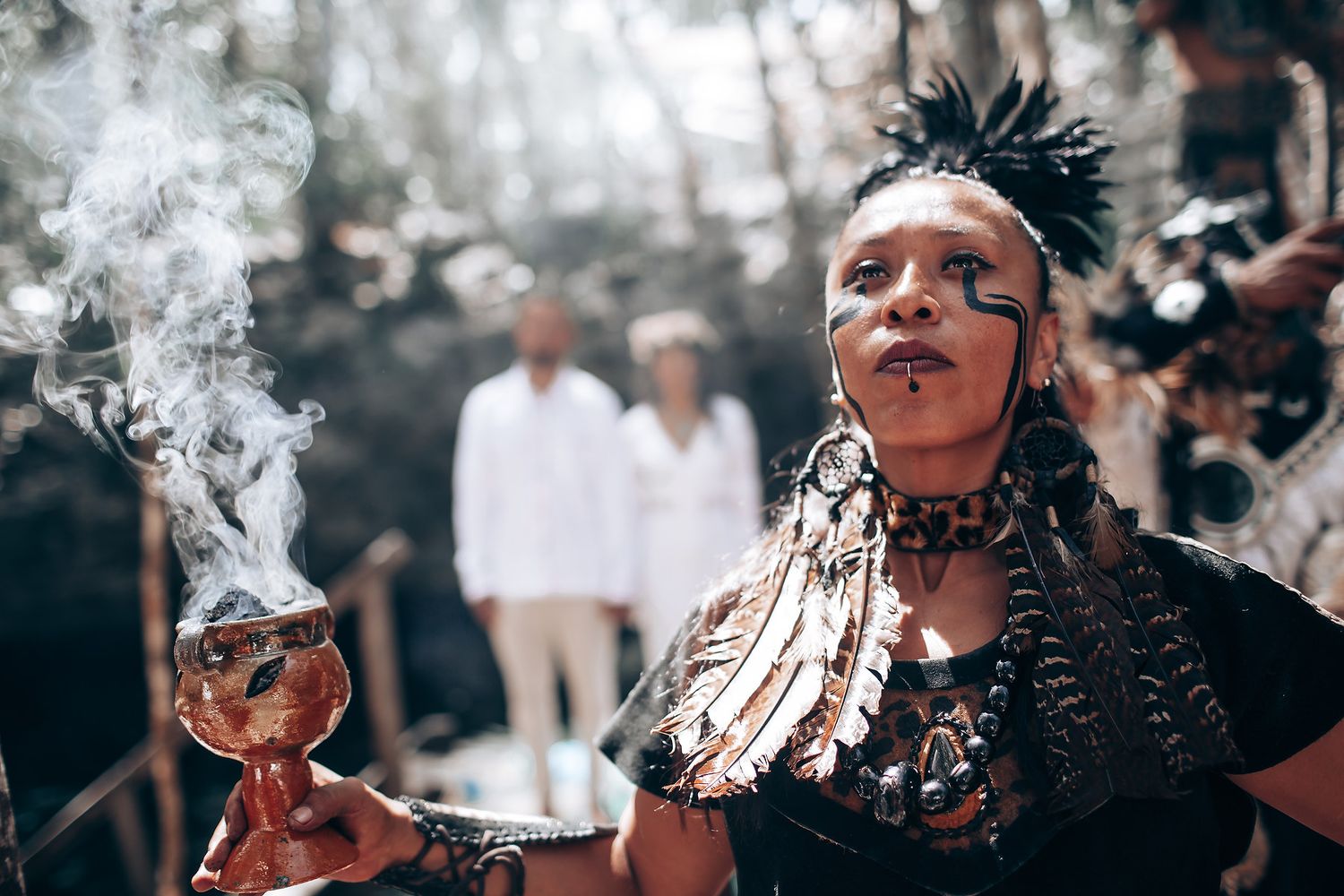 Smoke rises during a traditional spiritual ceremony as participants gather in nature.