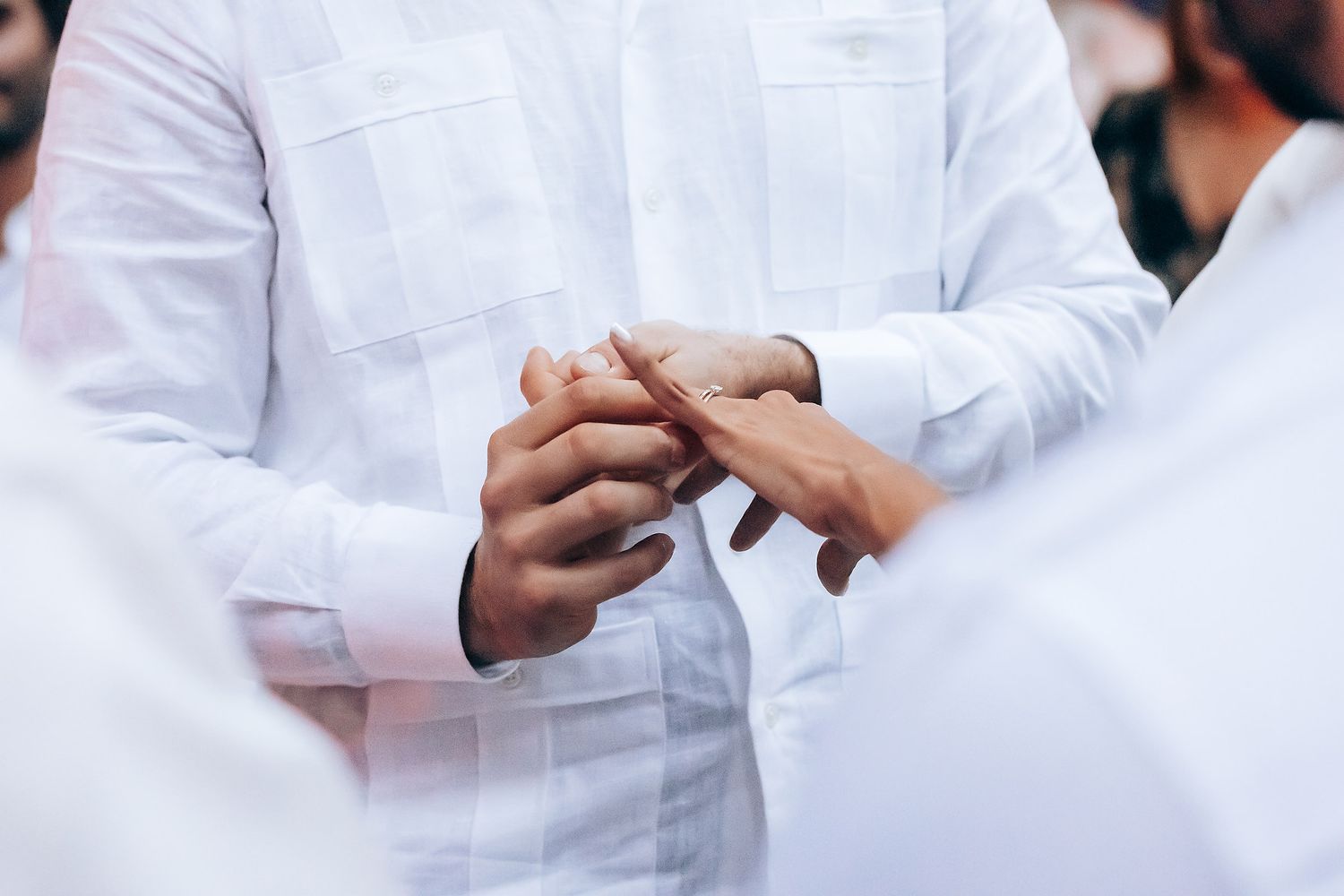 Close-up details of white formal attire and hands during a wedding ceremony.