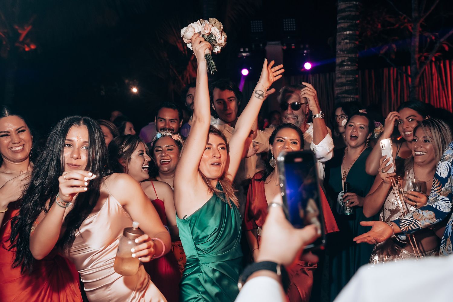 Lively crowd enjoying themselves under dramatic nightclub lighting with hands raised in celebration.