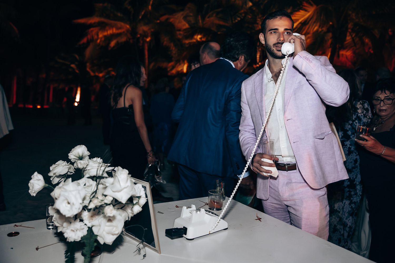 Someone in a pink suit smoking at an evening reception with floral decorations.