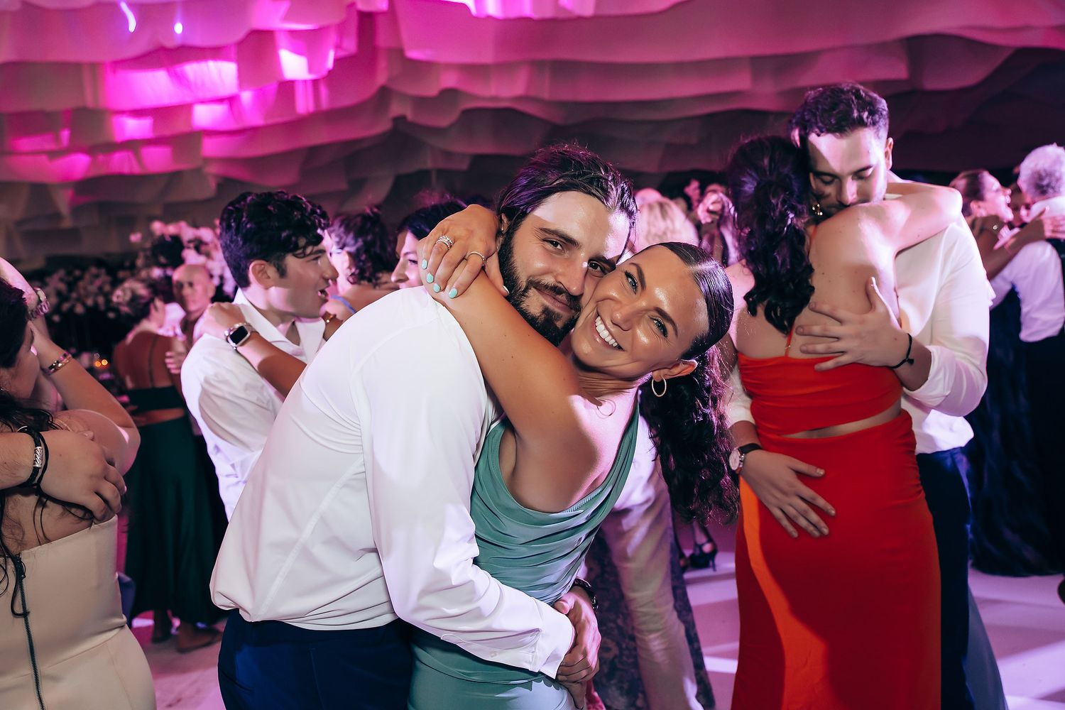People dancing together at a party venue illuminated by vibrant pink lighting.