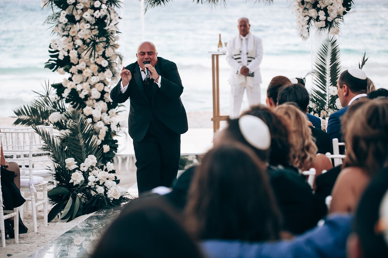 Beachfront wedding ceremony setup with white floral arrangements and ocean backdrop.