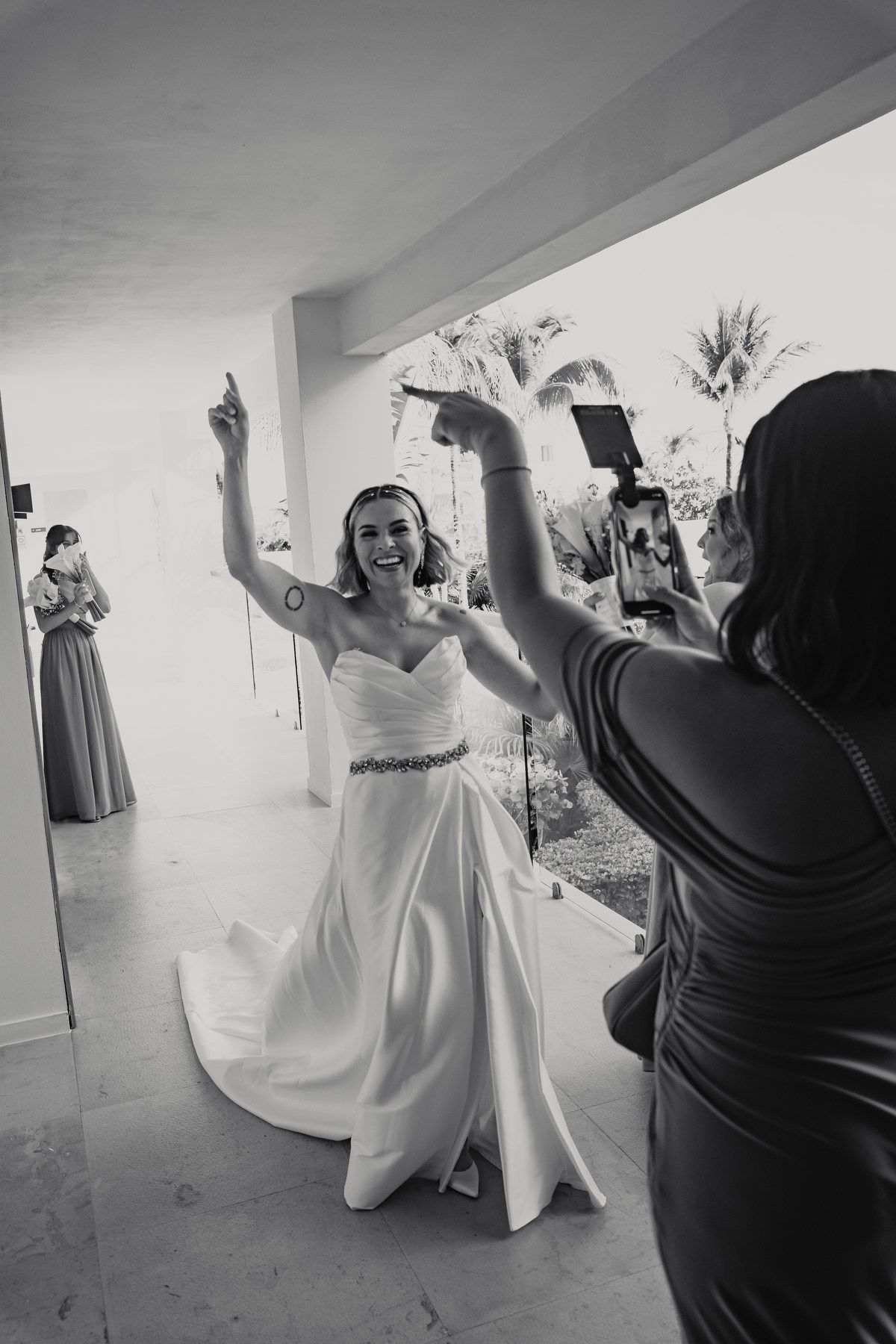 Joyful bride in white wedding gown dancing and celebrating with bridesmaids in black and white photo.
