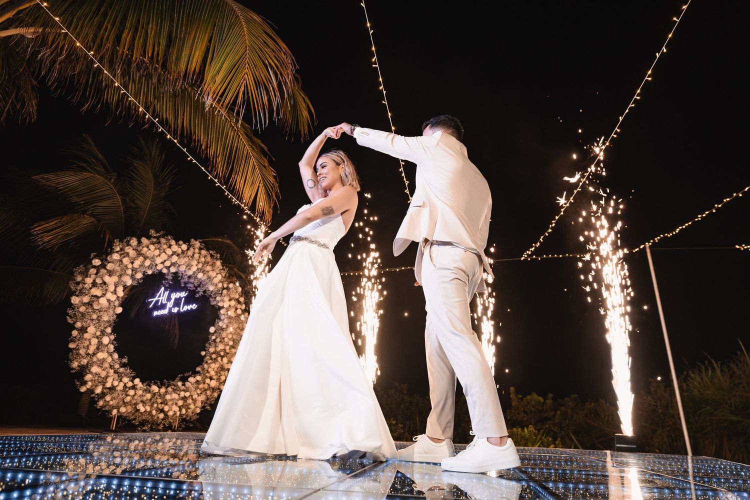 Bride and groom first dance surrounded by sparkling fountains and string lights at night reception.