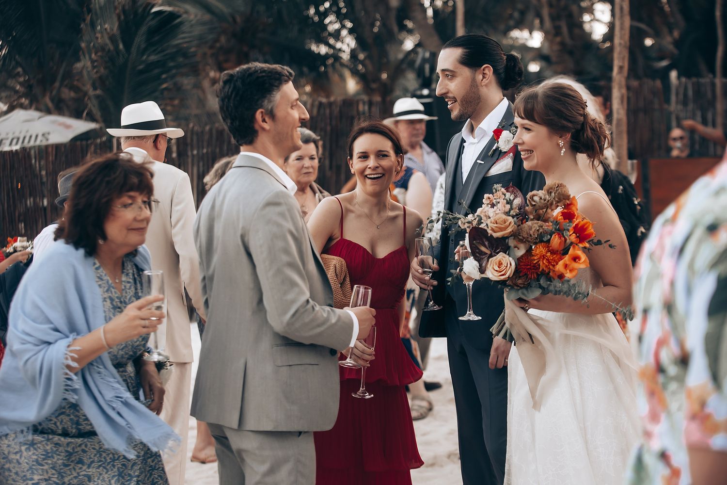 Guests enjoying a festive outdoor wedding reception under palm trees and twinkling lights.
