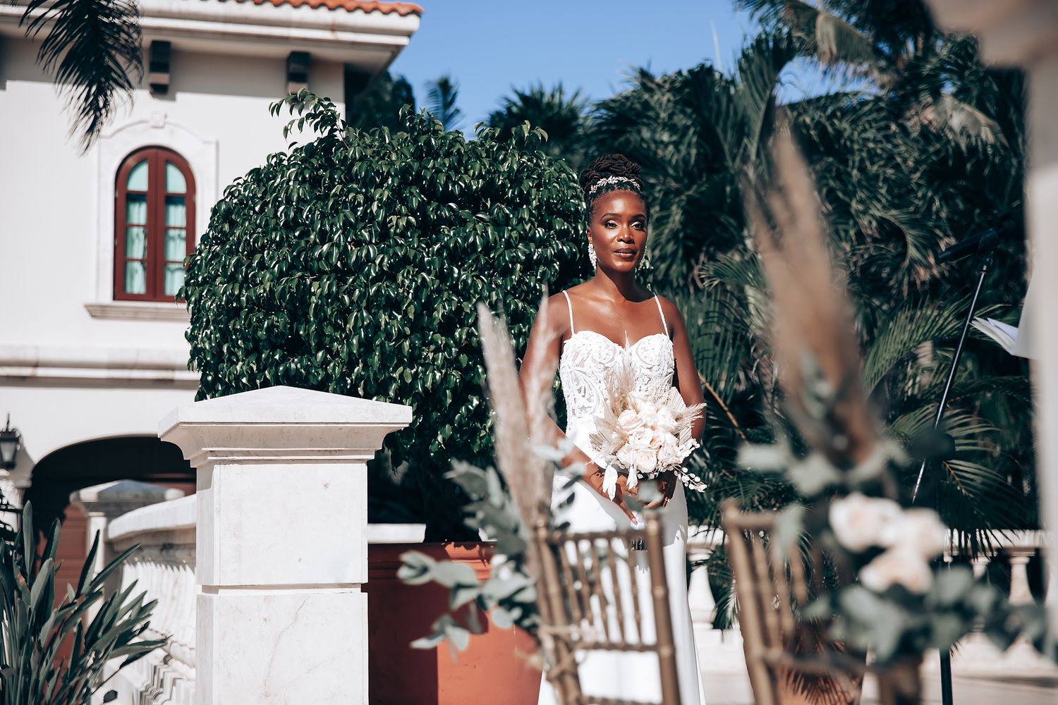 Elegant outdoor wedding venue with white pillars and palm trees under bright blue sky.