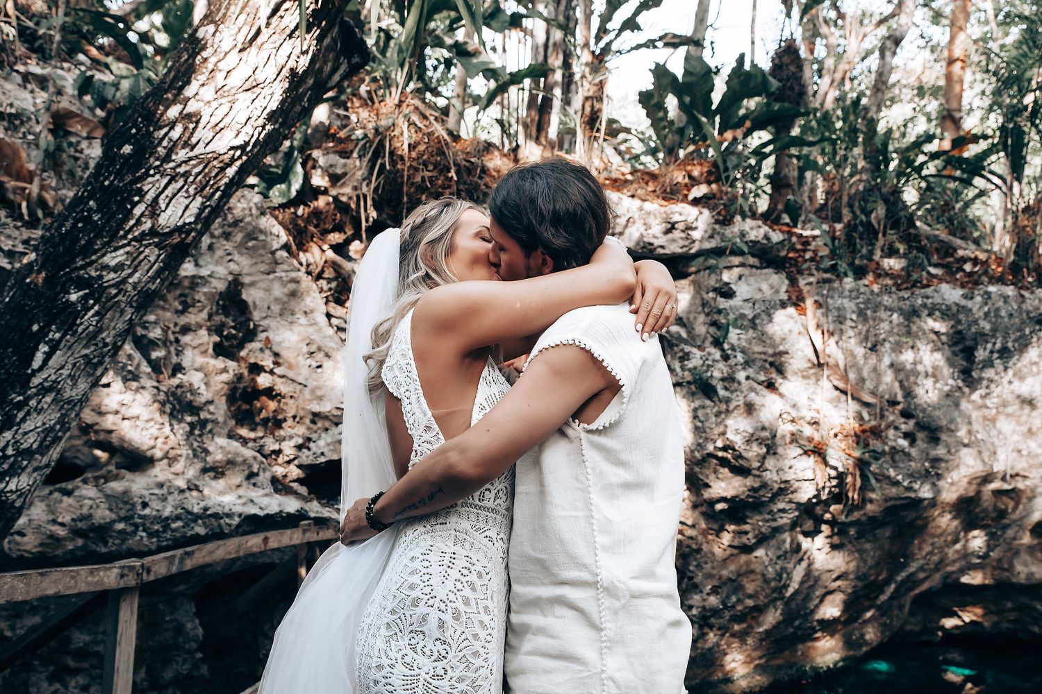 A romantic couple in white outfits embrace and kiss during an outdoor photo session against a rocky backdrop.