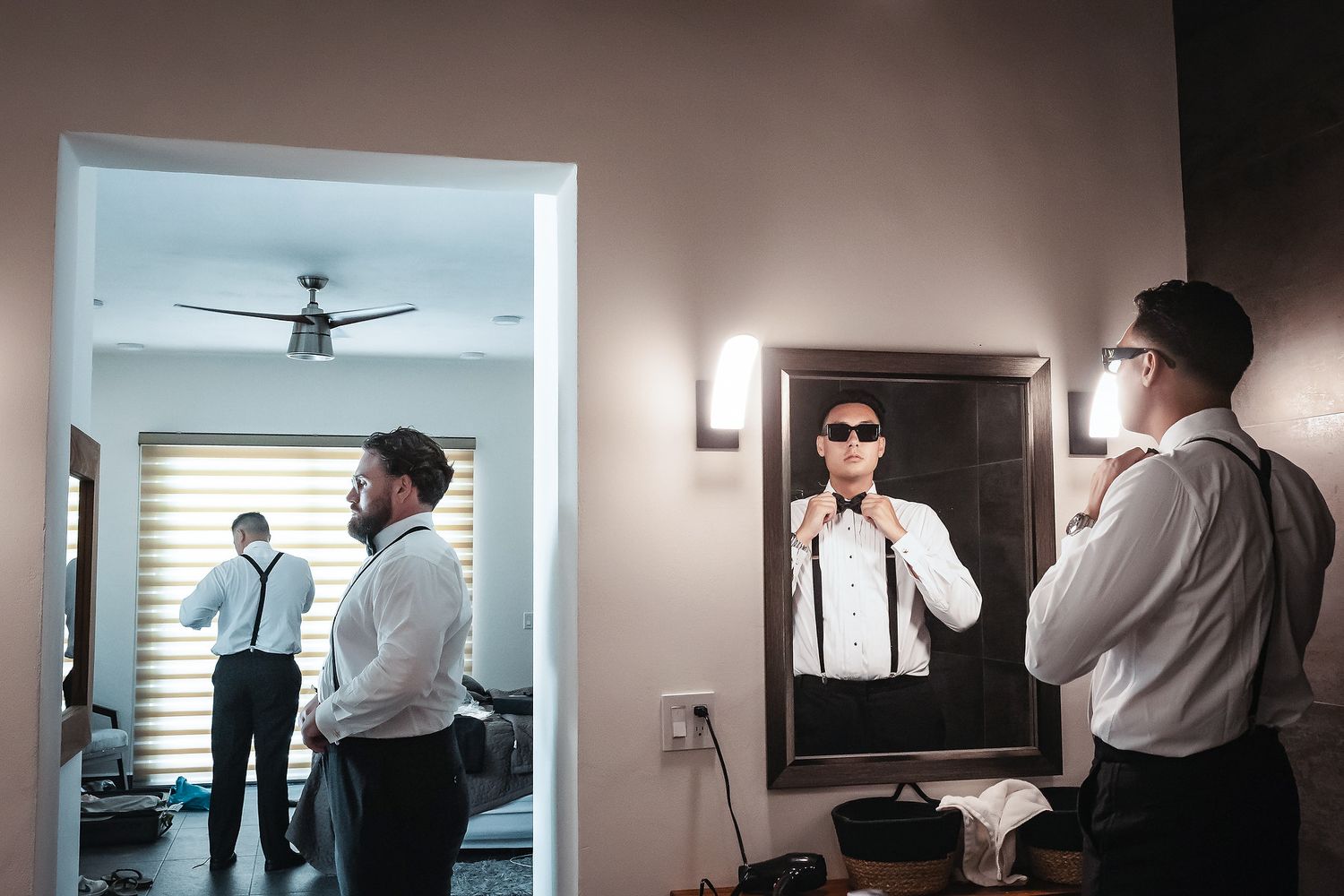 Groom adjusting his tie in a mirror reflection while getting ready in a stylish room with suspenders.