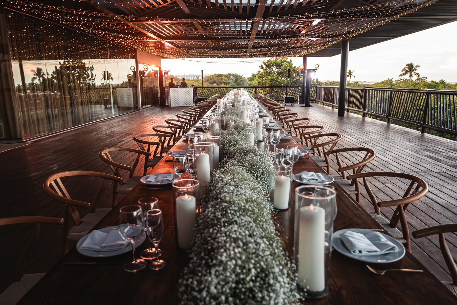 Elegant outdoor wedding reception with long table, baby's breath centerpiece, candles, and string lights at sunset.