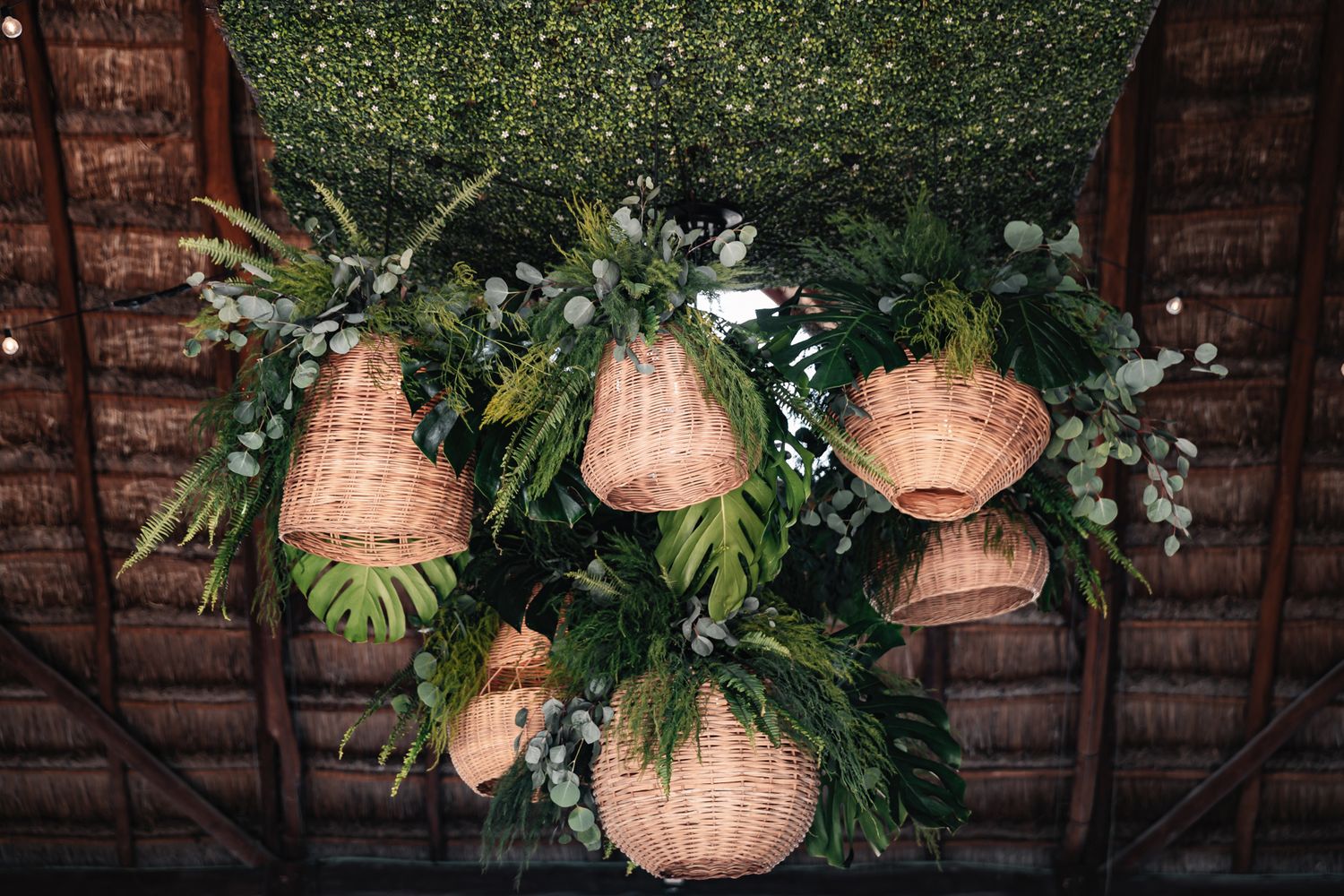 Wicker hanging baskets adorned with lush tropical greenery and eucalyptus displayed under a rustic wooden ceiling.