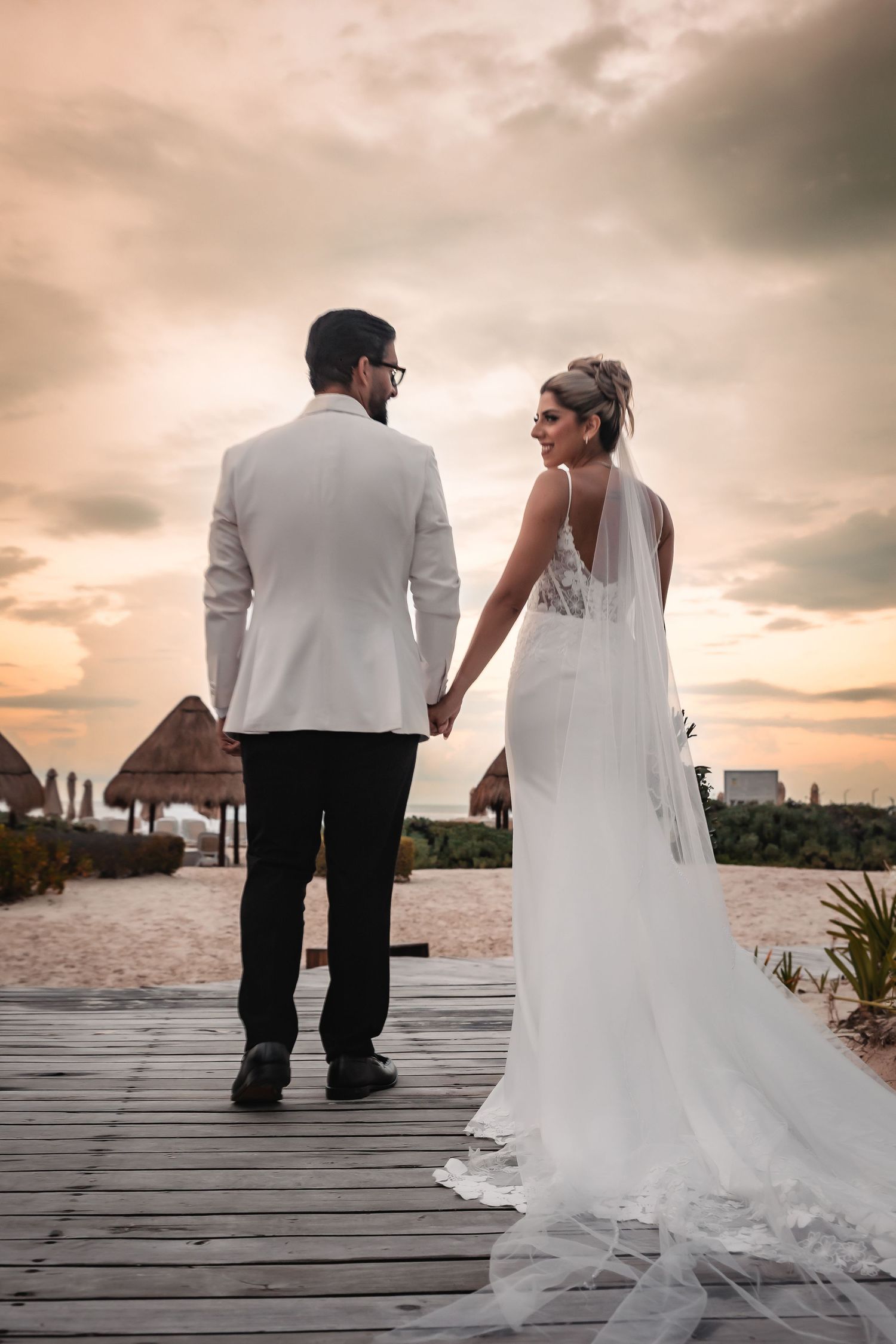 Newlyweds sit together on a wooden dock at sunset overlooking the ocean with flowing white wedding dress.