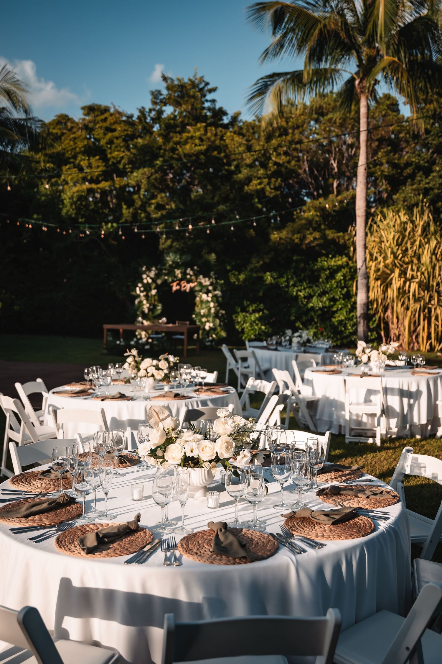 Elegant outdoor wedding reception tables set with white linens and tropical centerpieces.