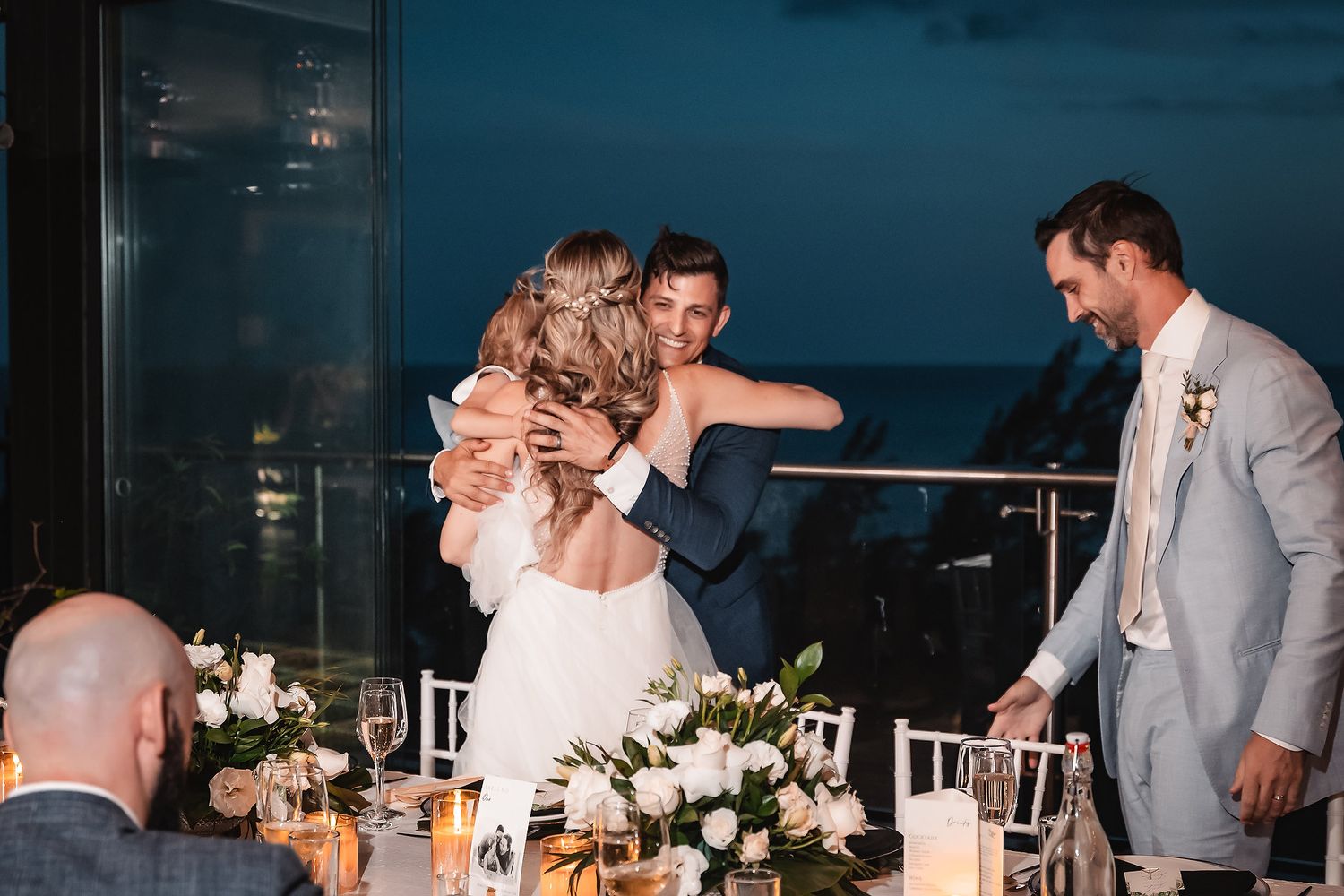 Emotional moment during wedding reception toasts at elegant oceanfront venue with floral centerpieces.