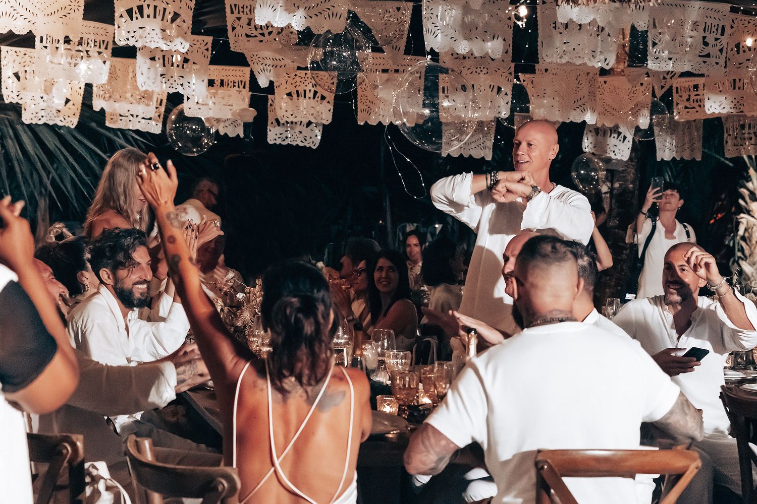 A crowded bar interior with patrons socializing and dancing while dollar bills cover the walls and ceiling.
