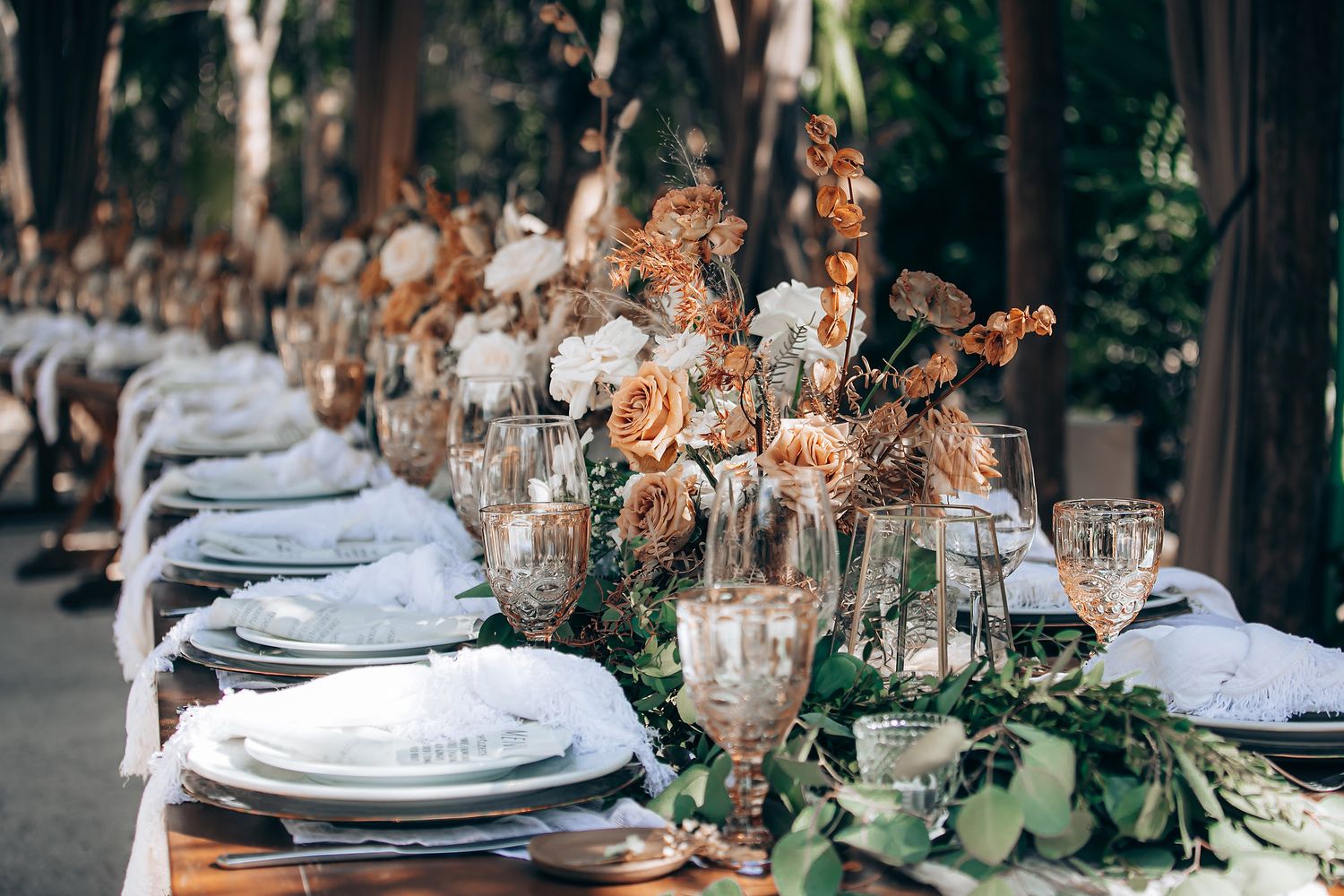 Elegant wedding table setting with crystal glasses, white plates, and delicate floral arrangements in muted tones.