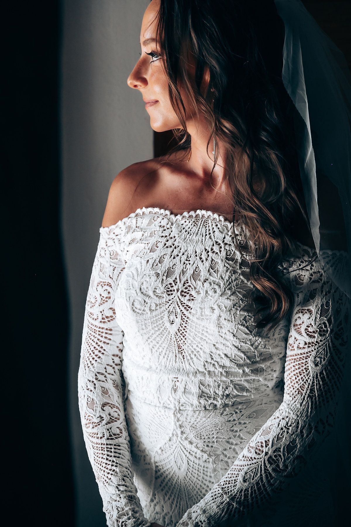 Close-up portrait of a delicate white lace wedding dress with intricate patterns and long sleeves.