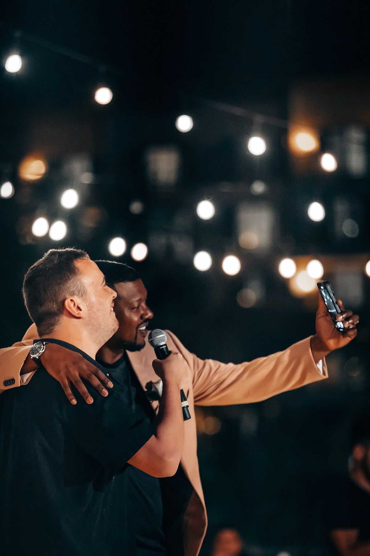 A group of people hugging and celebrating under ambient lighting at an evening event.