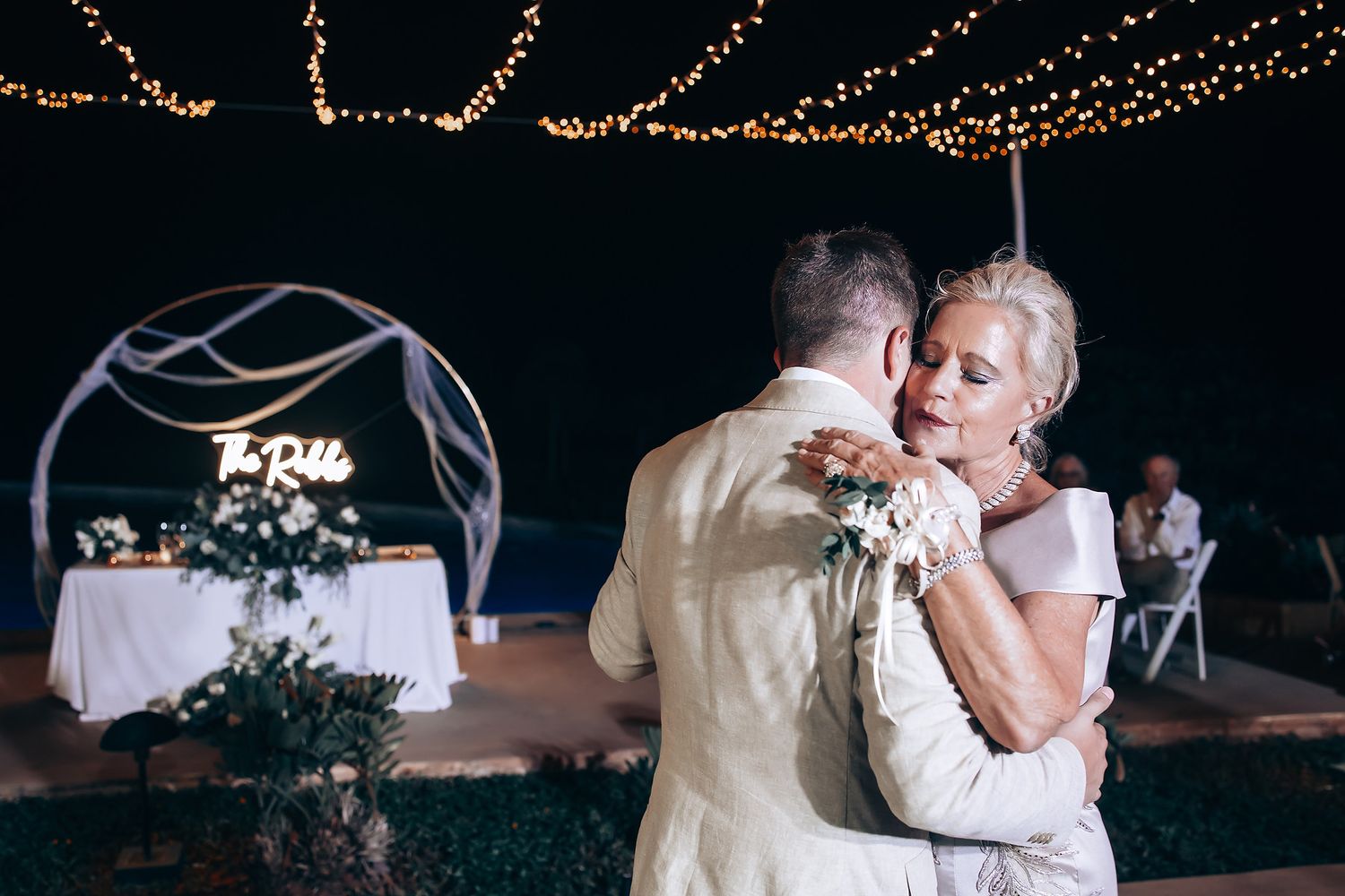 Romantic first dance under twinkling lights at evening wedding reception.