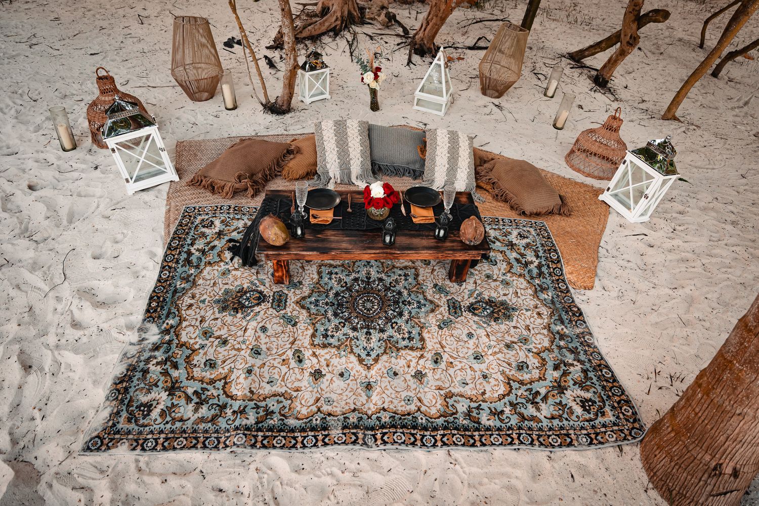 Overhead view of beach picnic setup with ornate rug and wooden benches.