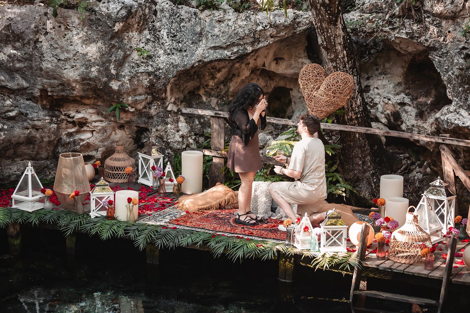 Decorative lanterns and ornaments arranged along rocky ledge beside turquoise cenote waters.