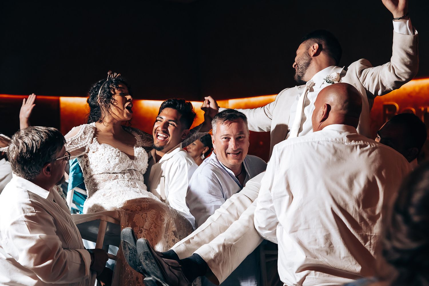 Wedding guests in white clothing dance and celebrate at an energetic reception party.